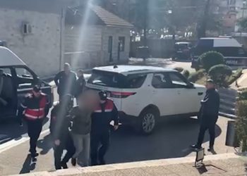 Me pranga në duar dhe duke çaluar nga këmba, momenti kur mbërrin në komisariat grabitësi i postës në Gjirokastër (VIDEO)