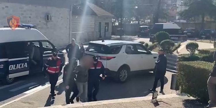 Me pranga në duar dhe duke çaluar nga këmba, momenti kur mbërrin në komisariat grabitësi i postës në Gjirokastër (VIDEO)